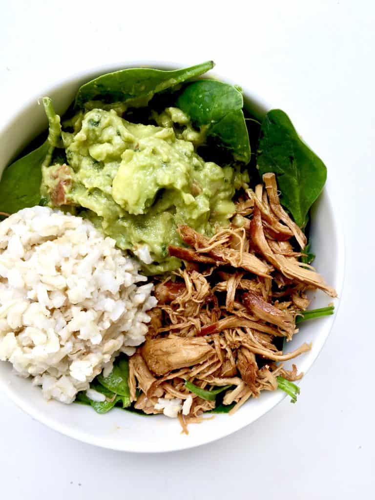 white bowl filled with rice, shredded crockpot honey garlic chicken, avocado, and spinach
