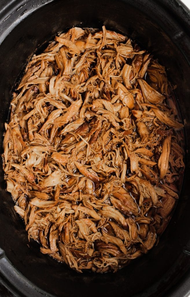 This Healthy 5 Ingredient Honey Garlic Chicken recipe takes no time to throw together using your crock-pot or slow cooker. Enjoy this super easy slow cooker recipe that's perfect for meal-prep, an easy weeknight dinner, or potluck! #crockpot #healthyrecipe #slowcookerrecipe #crockpotrecipe #slowcooker #honeygarlicchicken overhead shot of shredded honey garlic chicken in a black crockpot