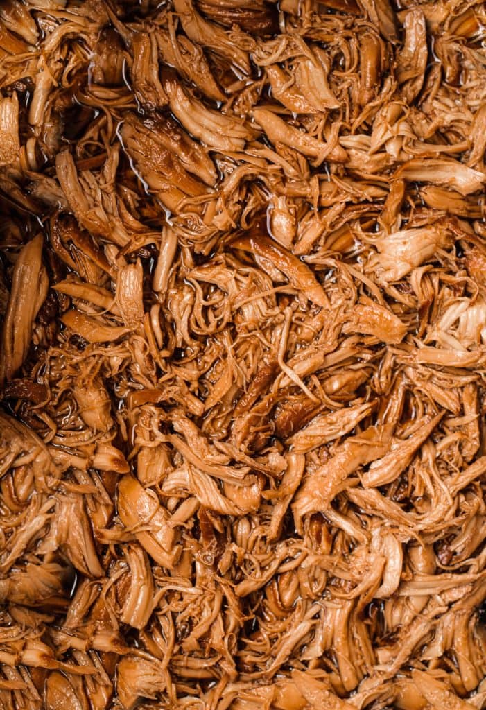 This Healthy 5 Ingredient Honey Garlic Chicken recipe takes no time to throw together using your crock-pot or slow cooker. Enjoy this super easy slow cooker recipe that's perfect for meal-prep, an easy weeknight dinner, or potluck! #crockpot #healthyrecipe #slowcookerrecipe #crockpotrecipe #slowcooker #honeygarlicchicken close up of shredded honey garlic chicken in juice