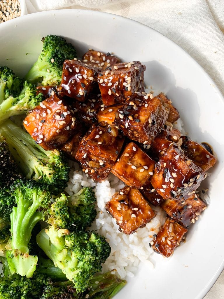 air fryer tofu with honey garlic sauce on a white plate next to broccoli