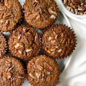 overhead shot of a plate of pecan pie muffins fresh out of the oven next to a bowl of pecans in a white bowl