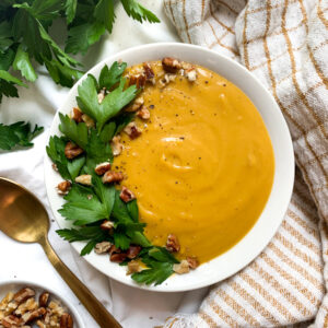 butternut squash soup with garnish next to spoon and pecans