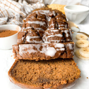 front view of healthy pumpkin banana bread loaf next to cup of cinnamon and sliced bananas