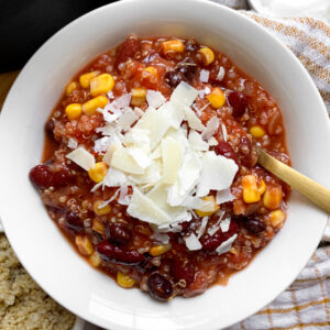 black bean chili with quinoa in a white bowl topped with cheese