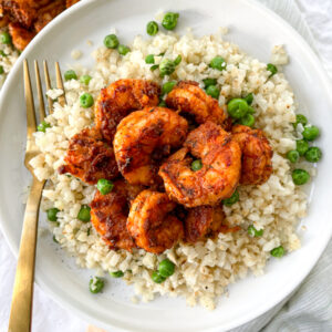 blackened shrimp over cauliflower rice on white plate with gold fork