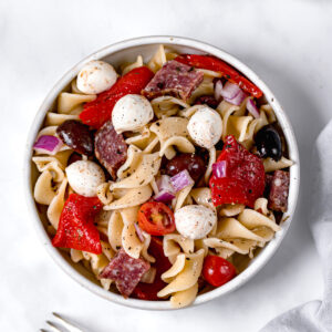italian pasta salad topped with mozzarella next to fork next to glass jar of dressing
