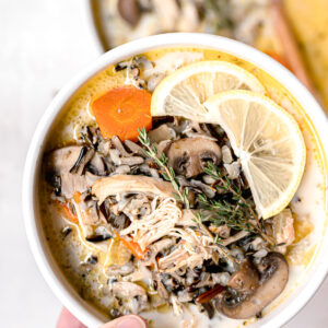 holding a bowl of instant pot wild rice soup with a lemon slice