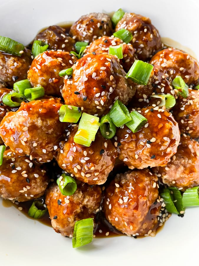 Close up of meatballs in white dish with sesame seeds and green onion