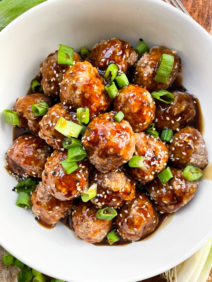 Asian chicken meatballs in a white bowl with green onions on top