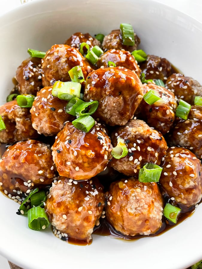 Stack of glazed meatballs in white dish with green onion and sesame garnish