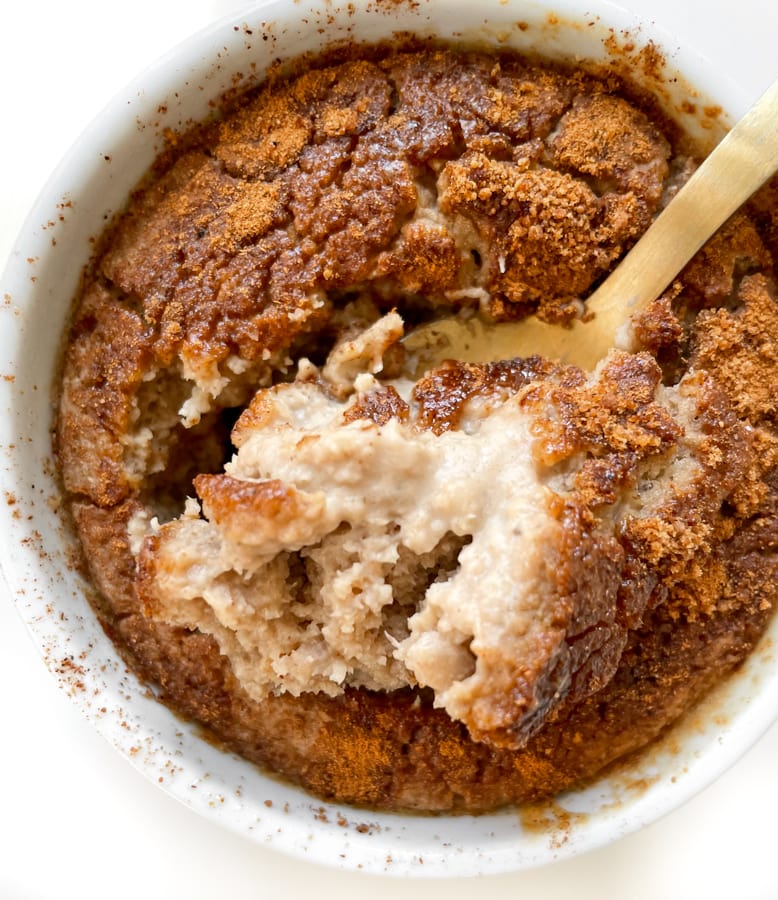 Overhead shot of snickerdoodle baked oats in a white ramekin with a gold spoon