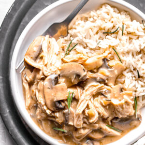 close up of mushroom chicken and rice with a fork on a white plate