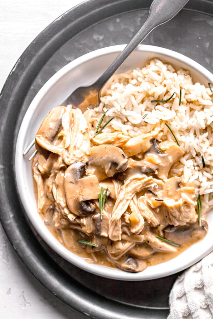close up of mushroom chicken and rice with a fork on a white plate