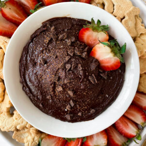 top shot of edible brownie batter in a white bowl on a plate with fruit and crackers
