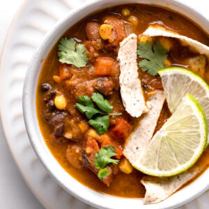 top shot of vegan taco soup in a white bowl topped with lime wedges