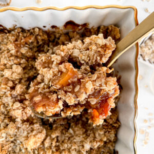 lifting a scoop of homemade peach crisp from a baking dish