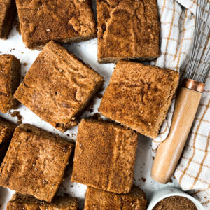 snickerdoodle bars next to cinnamon, a whisk, and a dish towel