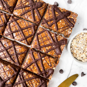 healthy Chocolate Peanut Butter Oatmeal Bars sliced into squares with chocolate drizzled on top next to oats and a gold knife