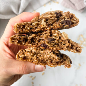 holding three halves of oatmeal raisin cookies