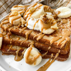 high protein french toast topped with nuts, sliced bananas, and drizzle of nut butter