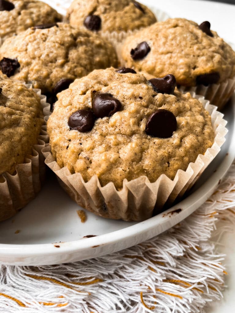 side view of oatmeal chocolate chip muffins on a white plate sitting on a dish towel