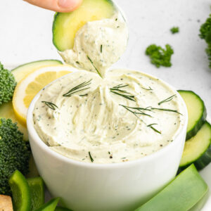dipping a cucumber in cottage cheese dip next to veggies.