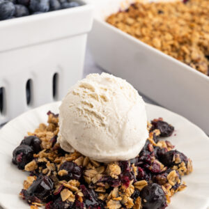 gluten free blueberry crisp on a white plate with a scoop of ice cream on top.