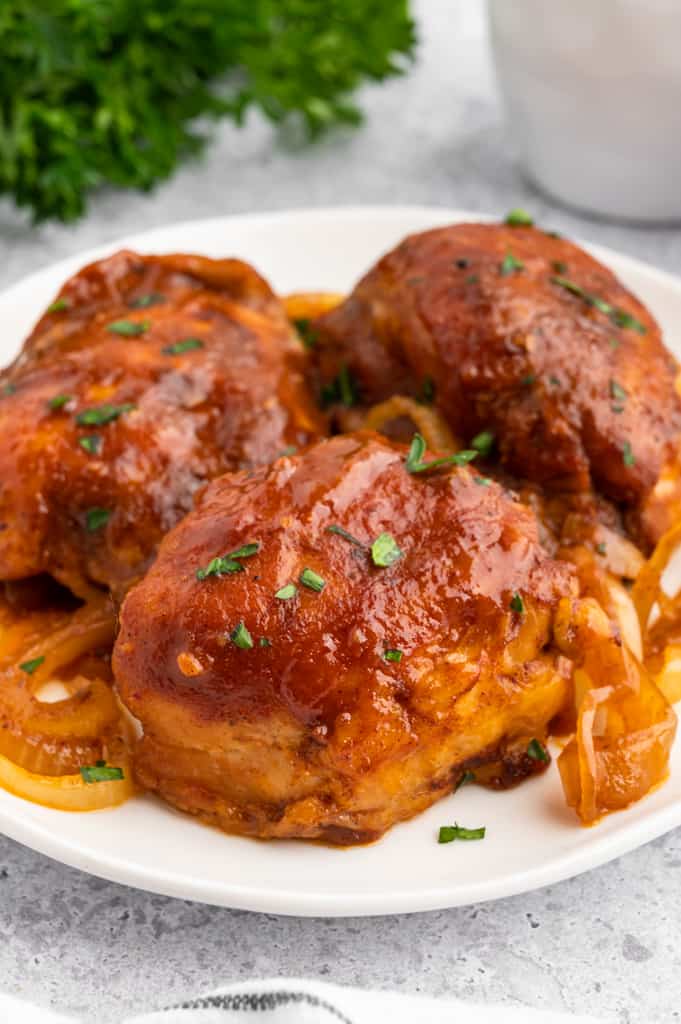 three bbq chicken thighs on a white plate.