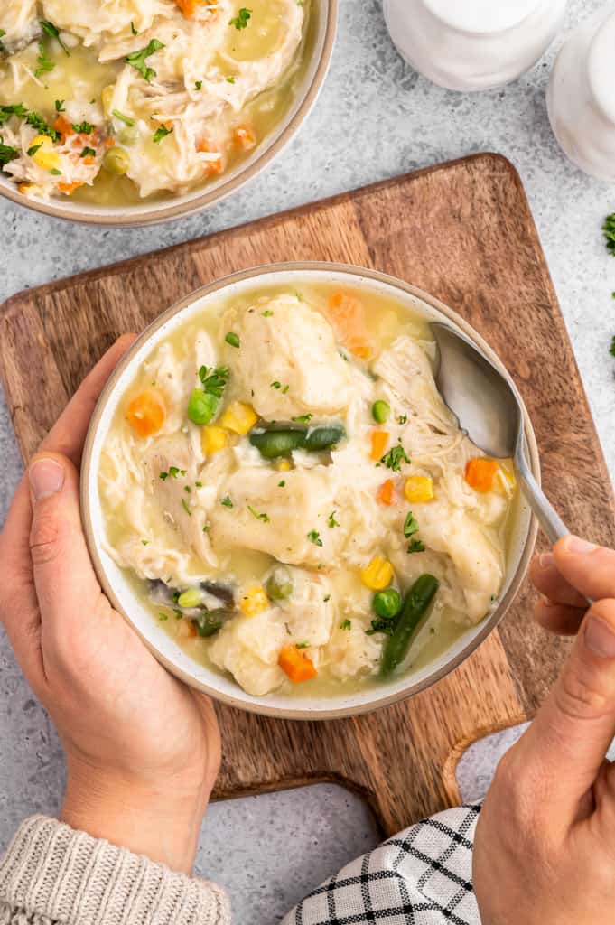 holding a bowl of slow cooker chicken and dumplings with a spoon in the bowl.