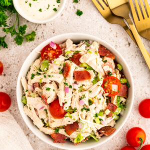 A bowl of BLT chicken salad next to forks and dressing.